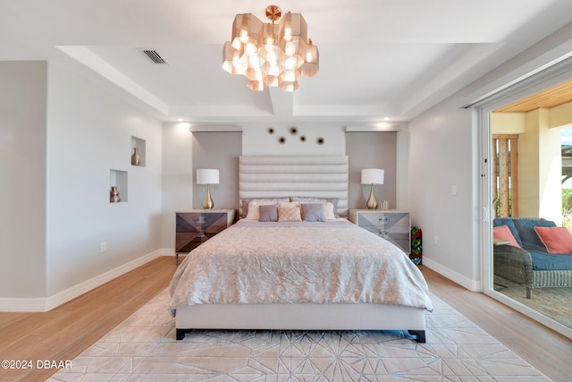 bedroom with a chandelier, light hardwood / wood-style flooring, and a tray ceiling