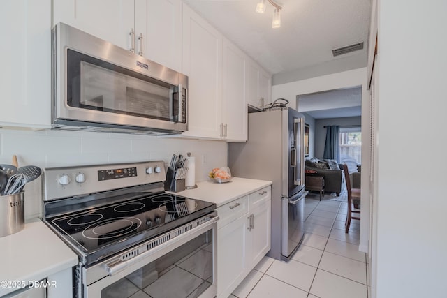 kitchen featuring a textured ceiling, white cabinets, stainless steel appliances, decorative backsplash, and light tile patterned flooring