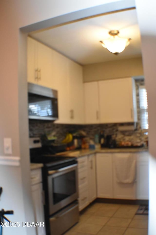 kitchen featuring decorative backsplash, appliances with stainless steel finishes, light tile patterned floors, and white cabinets