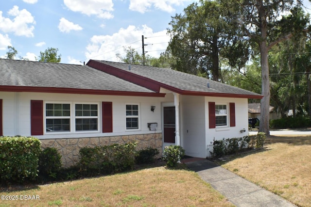 view of front of home featuring a shingled roof, a front lawn, and stone siding