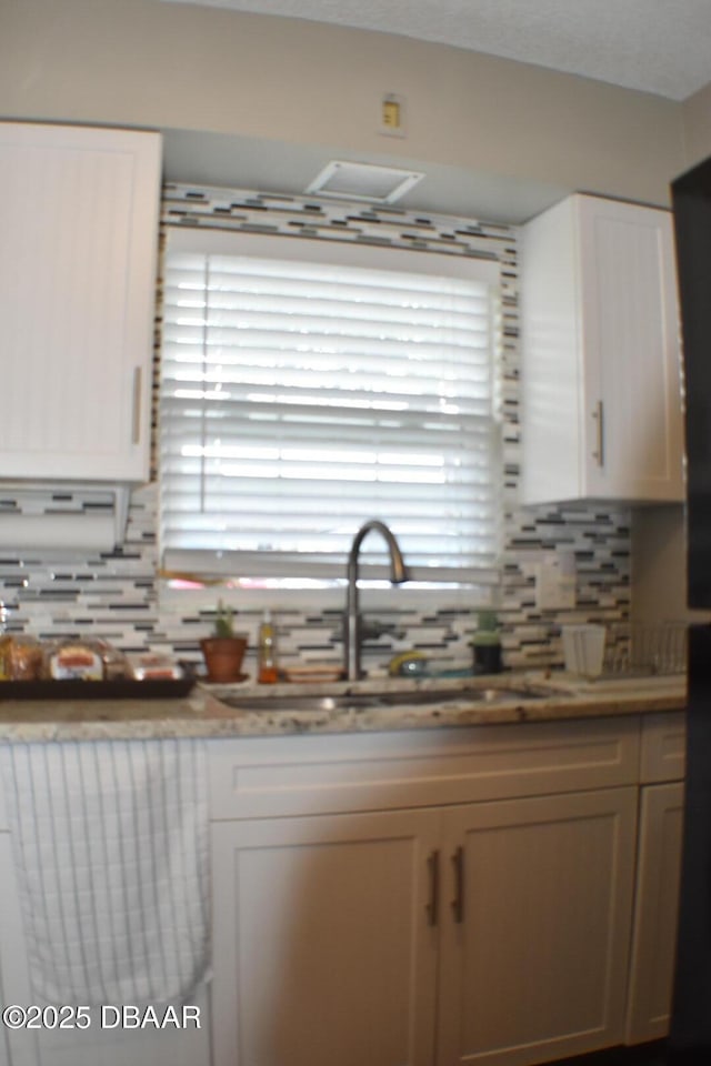 kitchen featuring a sink, light countertops, backsplash, and white cabinetry