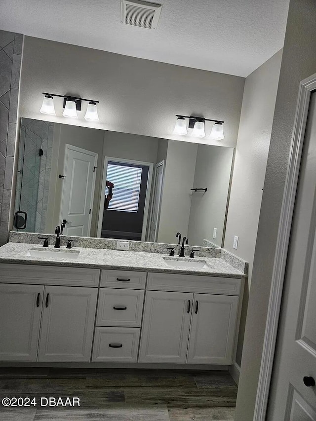 bathroom featuring a shower with shower door, wood-type flooring, vanity, and a textured ceiling