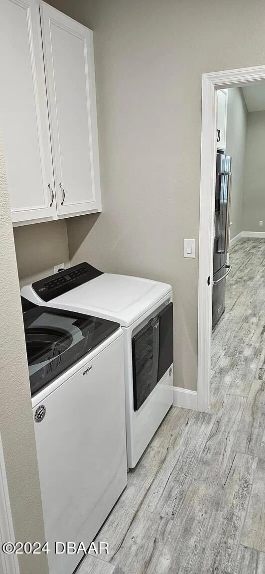 washroom with light wood-type flooring, cabinets, and washing machine and clothes dryer