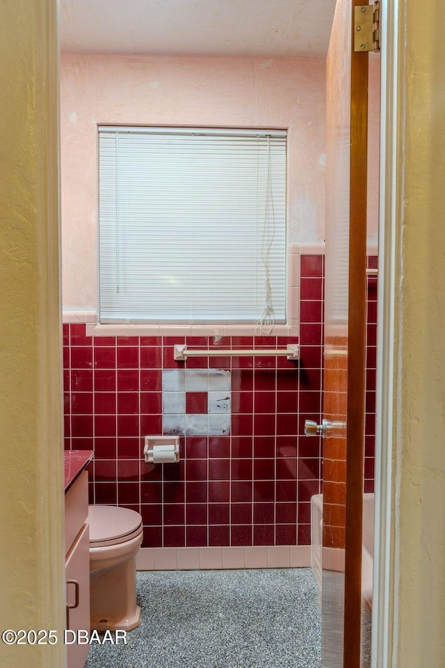 bathroom featuring toilet, vanity, tile walls, wainscoting, and a tub