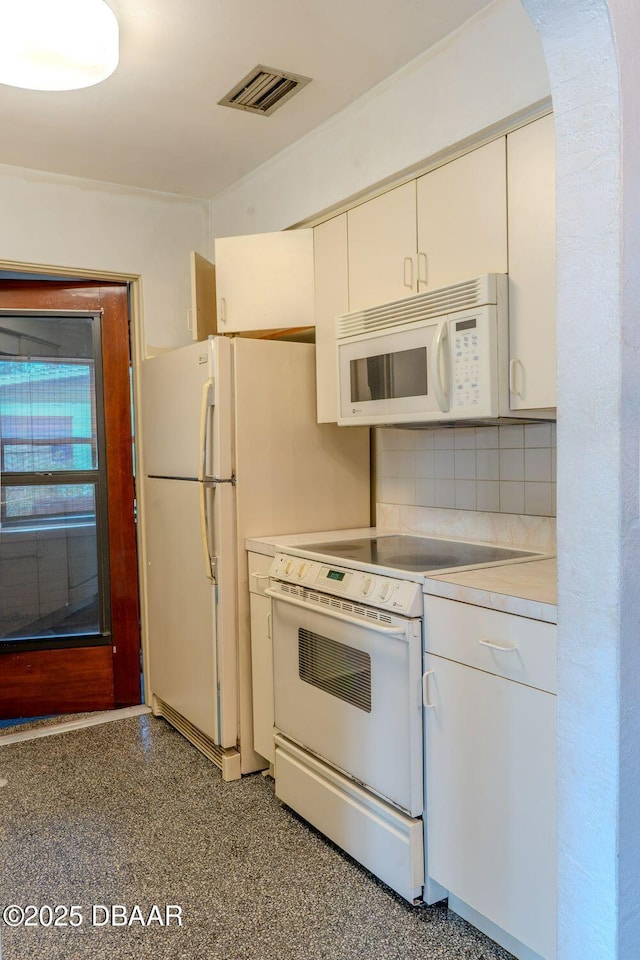 kitchen with white appliances, visible vents, white cabinets, light countertops, and decorative backsplash