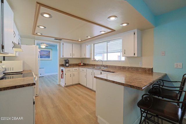 kitchen featuring light hardwood / wood-style floors, sink, kitchen peninsula, a kitchen breakfast bar, and white cabinets