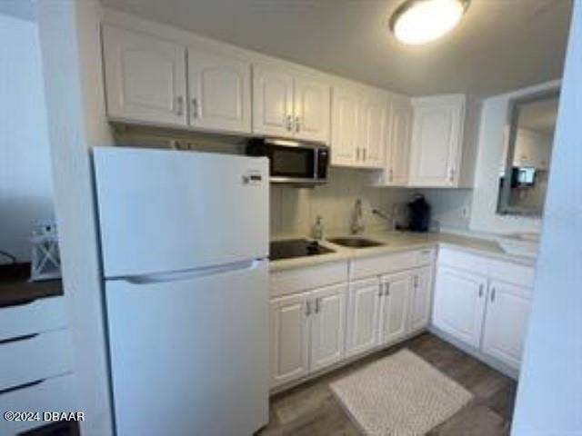 kitchen with hardwood / wood-style floors, sink, black stovetop, white fridge, and white cabinetry