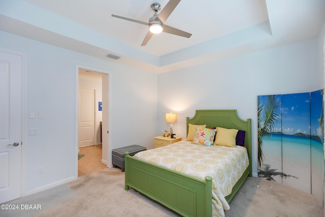 carpeted bedroom with a raised ceiling and ceiling fan