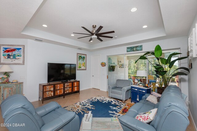 living room with light tile patterned floors, a tray ceiling, and ceiling fan