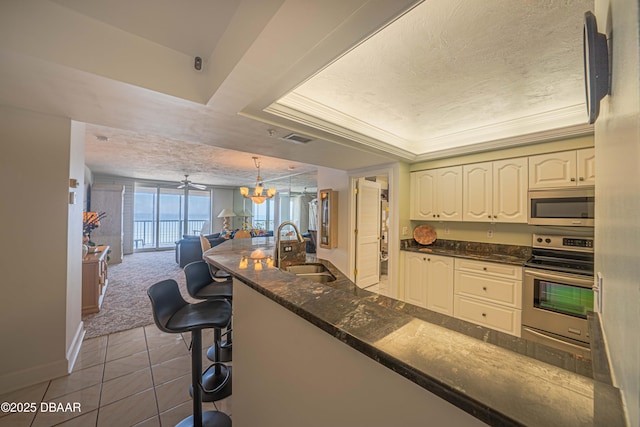 kitchen with pendant lighting, sink, a breakfast bar, appliances with stainless steel finishes, and a tray ceiling