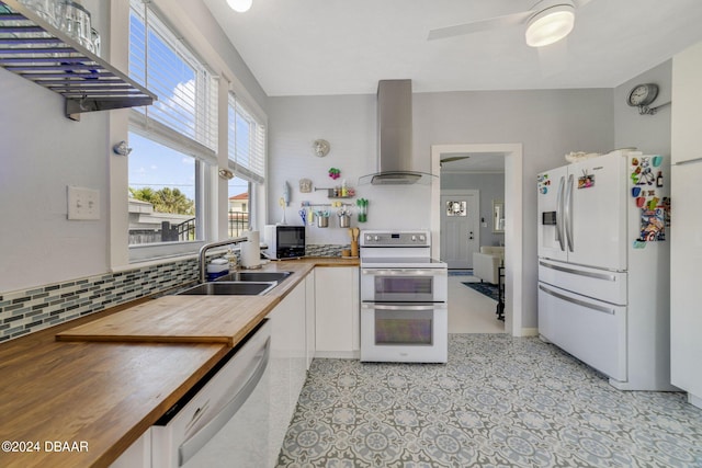 kitchen featuring decorative backsplash, wall chimney exhaust hood, white appliances, sink, and butcher block counters