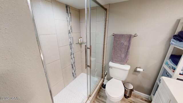 bathroom with hardwood / wood-style floors, toilet, and a shower with door