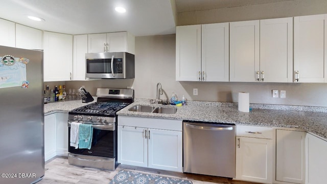 kitchen with appliances with stainless steel finishes, light wood-type flooring, white cabinetry, and sink