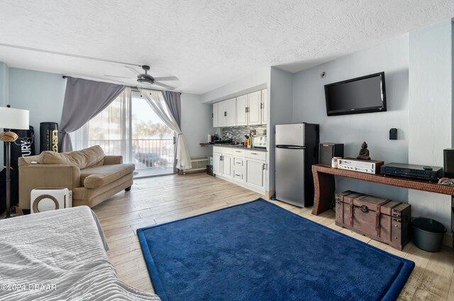 living room with light wood-type flooring, a textured ceiling, and ceiling fan