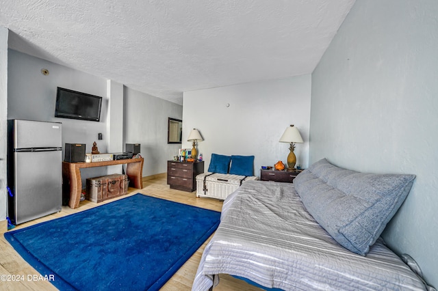 bedroom with hardwood / wood-style flooring, stainless steel refrigerator, and a textured ceiling