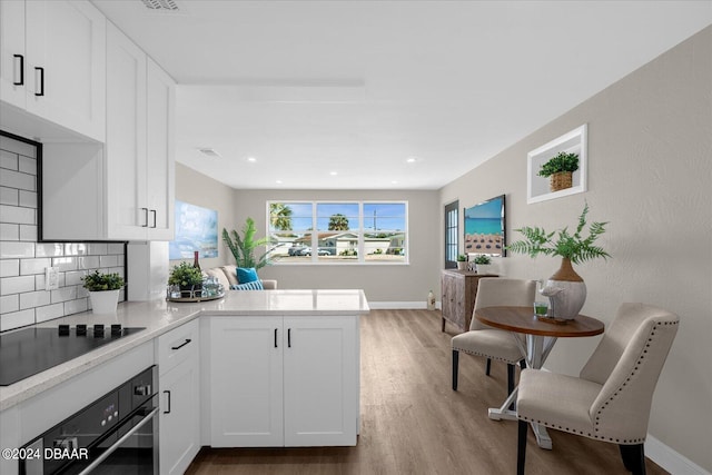 kitchen featuring light hardwood / wood-style floors, white cabinetry, black appliances, kitchen peninsula, and backsplash