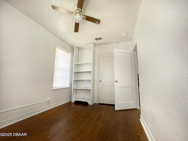 unfurnished bedroom with visible vents, ceiling fan, baseboards, dark wood finished floors, and a textured wall