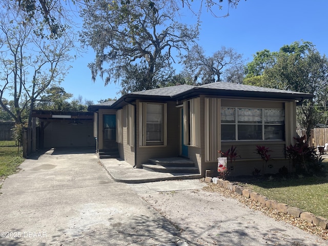 view of front of home featuring an attached carport, concrete driveway, fence, and a shingled roof