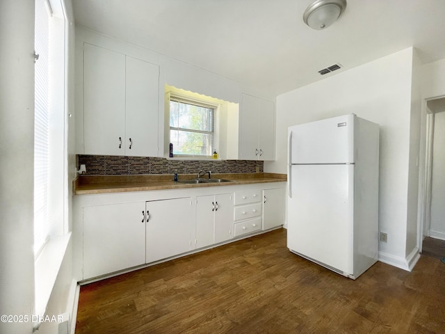 kitchen with visible vents, dark wood-type flooring, a sink, tasteful backsplash, and freestanding refrigerator