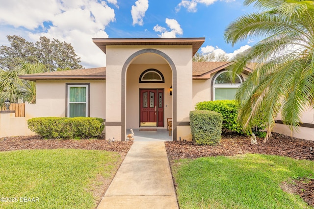 property entrance featuring a shingled roof, a lawn, and stucco siding