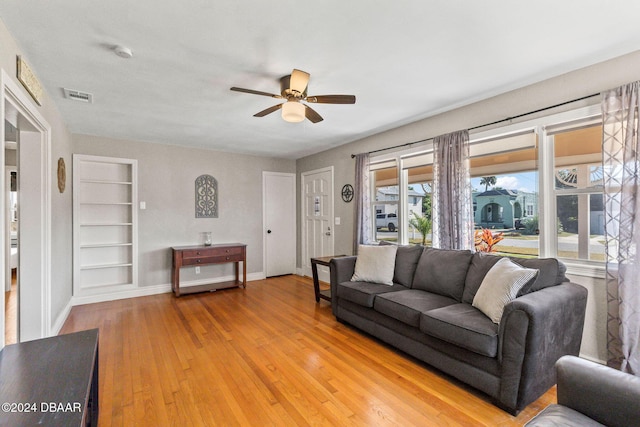 living room with built in shelves, ceiling fan, and hardwood / wood-style flooring