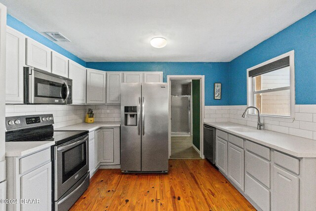 kitchen with decorative backsplash, light hardwood / wood-style floors, sink, and stainless steel appliances