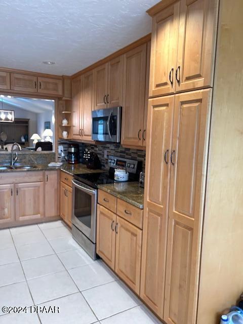 kitchen with stainless steel appliances, light tile patterned floors, backsplash, dark stone counters, and sink