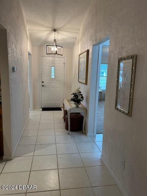 doorway featuring an inviting chandelier, lofted ceiling, and light tile patterned floors