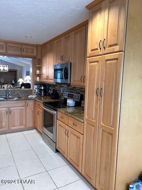 kitchen featuring stainless steel appliances, sink, dark stone countertops, light tile patterned floors, and decorative backsplash