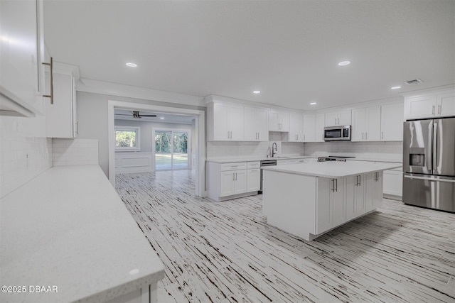 kitchen with appliances with stainless steel finishes, white cabinetry, decorative backsplash, sink, and a kitchen island