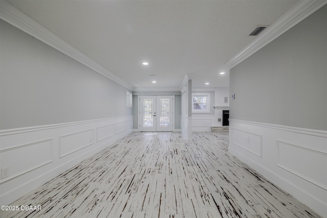 unfurnished living room with light wood-type flooring, crown molding, french doors, and a fireplace