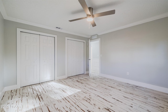 unfurnished bedroom with crown molding, light hardwood / wood-style floors, two closets, and ceiling fan