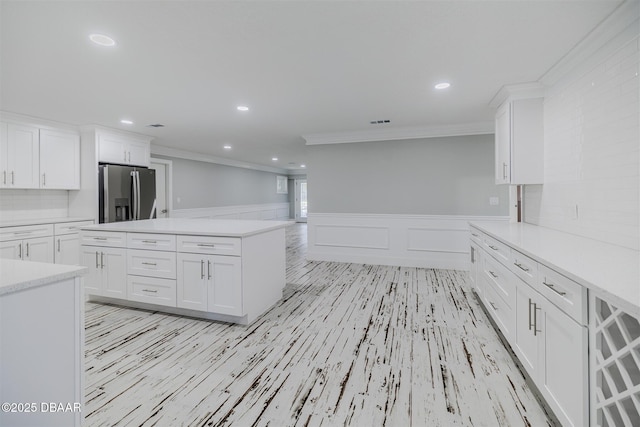 kitchen featuring white cabinetry, stainless steel refrigerator with ice dispenser, a kitchen island, ornamental molding, and backsplash