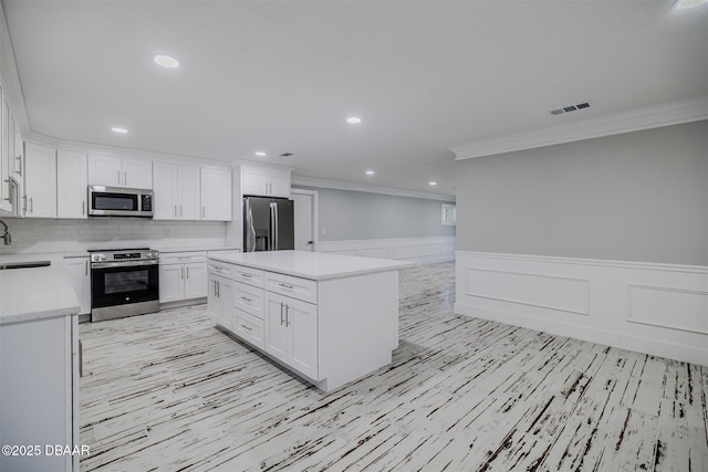 kitchen featuring crown molding, appliances with stainless steel finishes, tasteful backsplash, white cabinetry, and a kitchen island