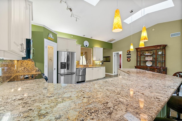 kitchen with lofted ceiling with skylight, appliances with stainless steel finishes, white cabinets, a kitchen bar, and hanging light fixtures