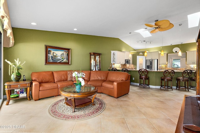 tiled living room featuring ceiling fan and vaulted ceiling with skylight