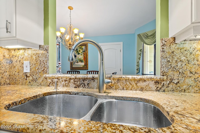 details featuring sink, tasteful backsplash, an inviting chandelier, light stone counters, and white cabinets