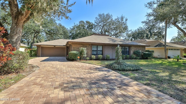 single story home featuring a front lawn, decorative driveway, brick siding, and an attached garage