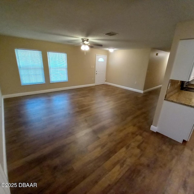 unfurnished living room featuring dark wood finished floors, visible vents, baseboards, and ceiling fan