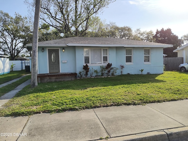 view of front facade featuring stucco siding, a shingled roof, a front lawn, and fence