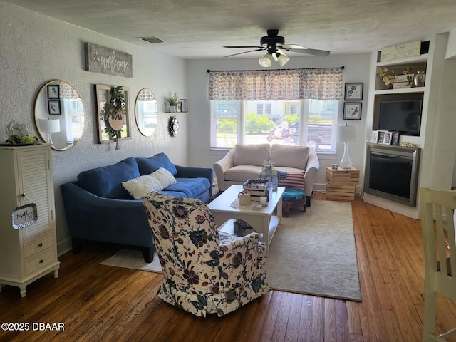 living area with a textured wall, visible vents, ceiling fan, and hardwood / wood-style flooring