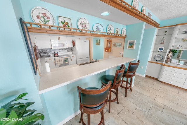 kitchen with kitchen peninsula, sink, a breakfast bar, white cabinetry, and white appliances