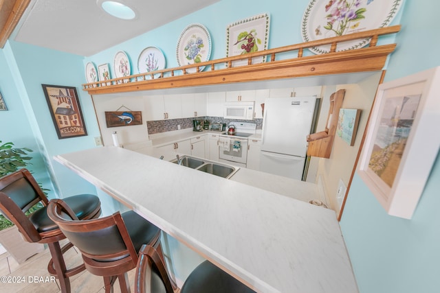 kitchen with tasteful backsplash, white cabinetry, kitchen peninsula, sink, and white appliances