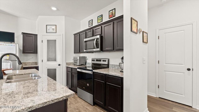 kitchen with dark brown cabinets, light stone countertops, light wood-style flooring, appliances with stainless steel finishes, and a sink