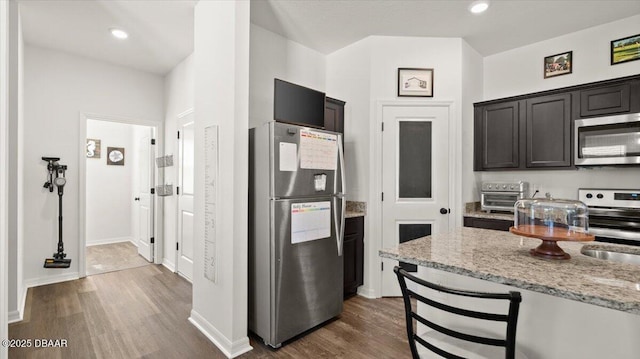 kitchen featuring light stone countertops, a breakfast bar, dark wood-style floors, stainless steel appliances, and a sink