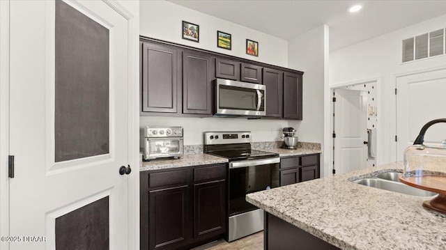 kitchen featuring visible vents, dark brown cabinets, light stone counters, appliances with stainless steel finishes, and a sink