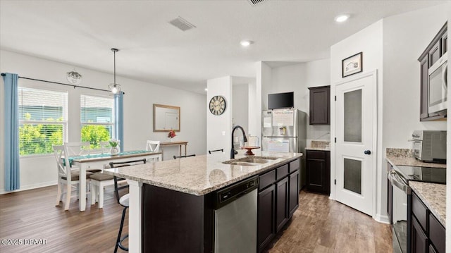 kitchen featuring visible vents, a center island with sink, wood finished floors, stainless steel appliances, and a sink