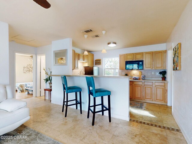 823 E 10th Ave, New Smyrna Beach, FL 32169 - kitchen featuring black microwave, a breakfast bar, decorative backsplash, freestanding refrigerator, and a peninsula