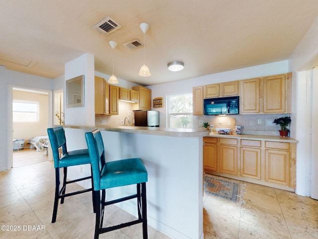 823 E 10th Ave, New Smyrna Beach, FL 32169 - kitchen with black microwave, light brown cabinetry, backsplash, freestanding refrigerator, and a kitchen breakfast bar
