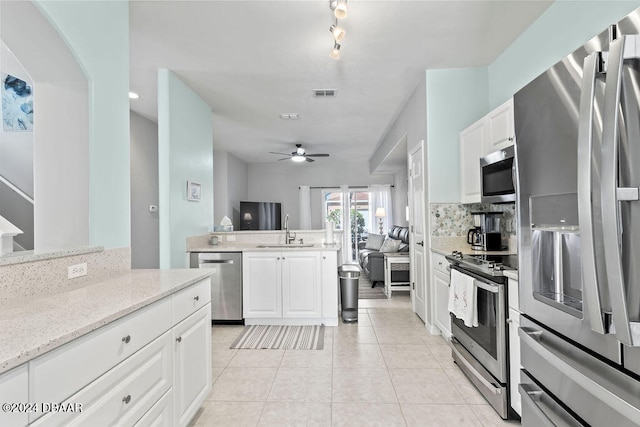 kitchen with appliances with stainless steel finishes, light tile patterned floors, light stone countertops, sink, and white cabinets